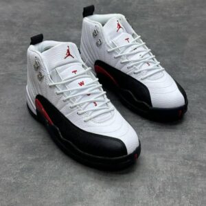A pair of white, black, and red Air Jordan 12 Retro sneakers on a grey background, showcasing the iconic design and sleek details.