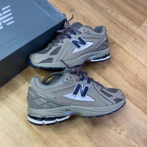 A pair of grey New Balance 990v6 sneakers on a wooden floor next to a shoe box, showcasing the shoe's sleek design and comfortable features.