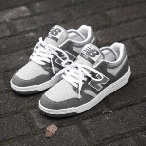 A pair of grey and white New Balance 480 sneakers on a brick background, showcasing their sleek design and comfortable features.