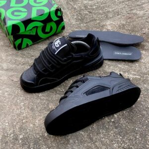A pair of black Dolce & Gabbana sneakers with box and insoles on a concrete surface, showcasing luxury footwear.