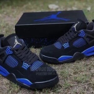 A pair of black and blue Air Jordan 4 sneakers placed on grass with the shoe box in the background, showcasing the sleek design and vibrant colors.