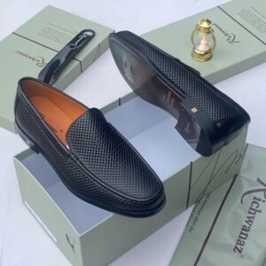 A pair of black woven leather loafers on a shoe box with accessories