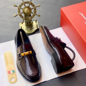 A pair of luxurious dark brown leather loafers on a white background, with a red shoe box and a golden ship's wheel in the background, showcasing high-class products for the elite at Levonteluxe in Nigeria.