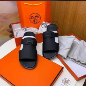 A pair of black double-buckle slide sandals with an orange box and bag, perfect for luxury footwear lovers in Nigeria.