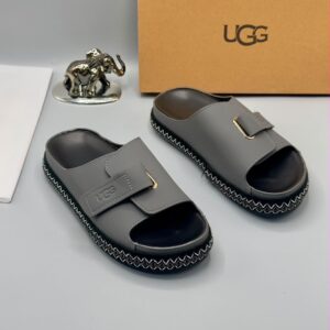 A pair of luxury grey UGG slide sandals displayed on a clean surface, with a golden elephant statue and UGG box in the background, showcasing high-class products for the elite in Nigeria.