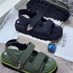 Luxurious chunky sandals in black and green, featuring two straps and a silver buckle, displayed on a wooden surface with brand packaging.