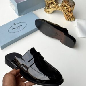 A pair of luxurious black half shoes showcased with their box and a golden decorative item, highlighting the shoe's sleek design and high-end packaging.