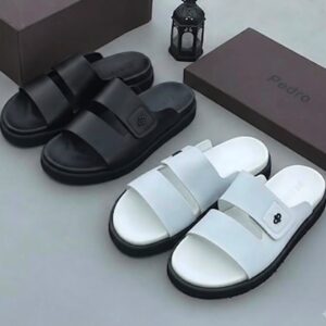 A pair of black and white Pedro slides, elegantly displayed on a pristine surface, accompanied by a brown shoe box and a sophisticated lantern, epitomizing luxury and refinement.