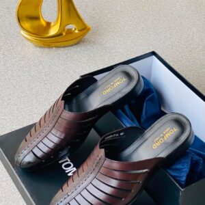 A pair of luxurious TOMFORD shoes in dark brown leather, presented in a black box with blue velvet lining, alongside a gold sculpture.