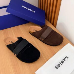 A pair of black and brown Birkenstock half shoes on a wooden table with a blue box and white bag.
