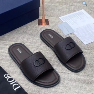 A pair of luxurious Dior slides with a sleek design and iconic logo, presented with a navy blue box and accessories on a light grey surface.