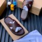 A pair of rich brown leather slides on top of shoe boxes with a white cloth bag, exuding luxury and comfort.