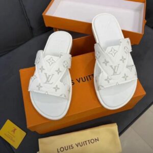 A pair of luxurious white Louis Vuitton slides with monogram pattern, placed on an orange shoe box and accompanied by a dust bag.