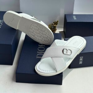 A pair of white leather slides with a silver 'CD' logo, placed on navy blue boxes with 'DIOR' embossed in white.