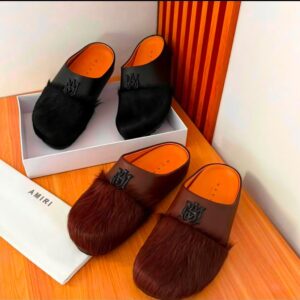 Luxurious mule slides in black and brown, featuring premium materials and distinctive logo, set against a sleek wooden backdrop.