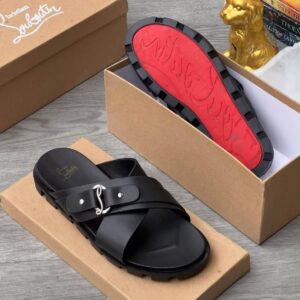 A pair of luxurious black Christian Louboutin sandals with a red sole, nestled in a brown shoe box alongside a golden dog statue and books.