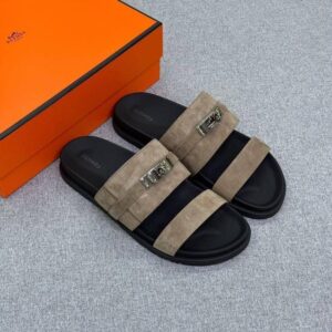 A pair of luxurious Hermes slides with black soles and tan straps, accompanied by an orange box, showcasing exceptional craftsmanship and style.